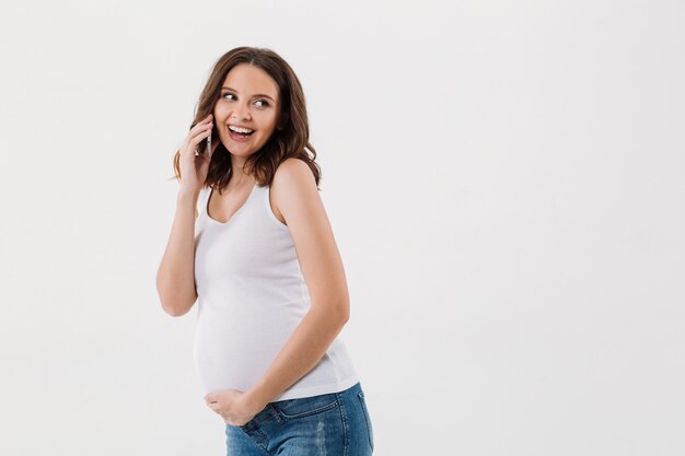 Glimlachende zwangere vrouw die door mobiele telefoon spreekt