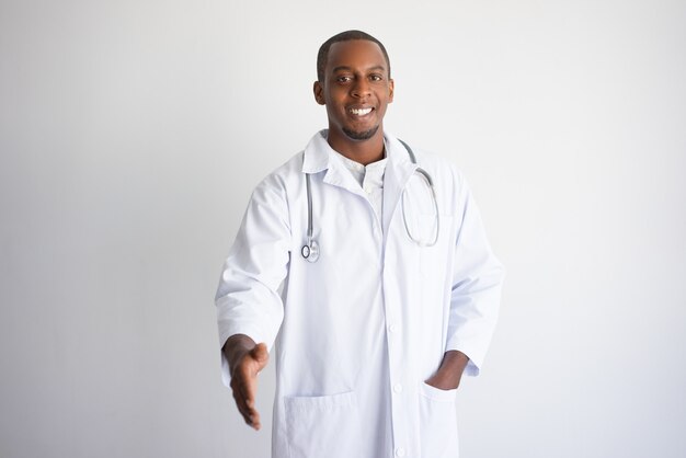 Glimlachende zwarte mannelijke arts die wapen voor handdruk uitbreidt.