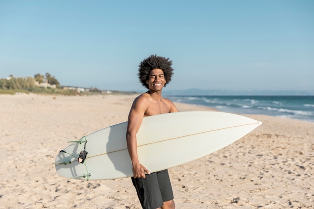 Glimlachende zwarte mens met surfplank op kust