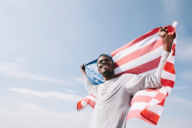 Glimlachende zwarte mensenholding die Amerikaanse vlag achter rug golven