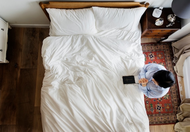 Godsvruchtige vrouw met een bijbelboek dat bij het bed bidt