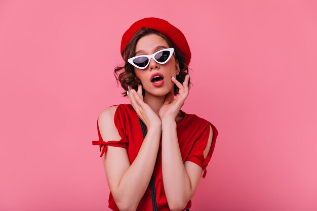 Goed uitziend vrouwelijk model in Franse outfit grappig poseren op lichte achtergrond Studio shot van sensueel wit meisje in rode baret