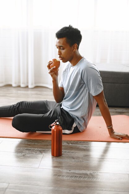 Goede voeding, gezonde levensstijl. Jonge fit sportieve man blogger appel eten voor lichte snack. Woonkamer, gezellig huis.