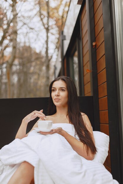 Goedemorgen. Vrouw in een deken. Dame zittend op terras. Brunette drinkt een kop koffie.