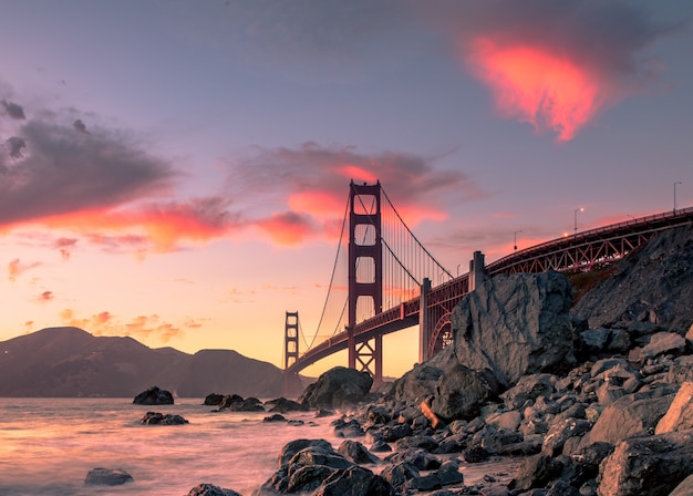 Golden gate bridge op watermassa dichtbij rotsvormingen tijdens zonsondergang in San Francisco, Californië