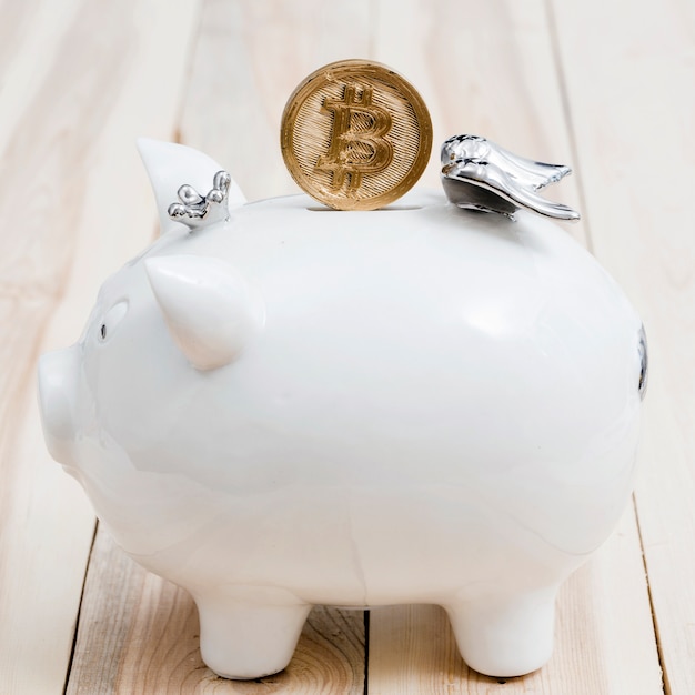 Gouden bitcoins over de groef van witte piggybank op houten lijst