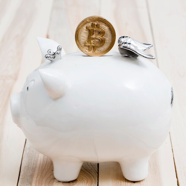 Gouden bitcoins over de groef van witte piggybank op houten lijst