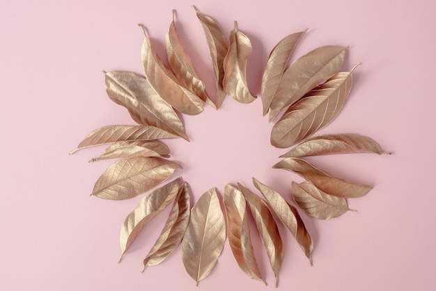 Gouden bladeren geplaatst in een cirkelframe op een roze achtergrond