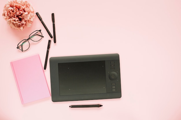 Gratis foto grafische digitale tablet; viltstiften; oogglazen en roze notitieboekje op roze achtergrond