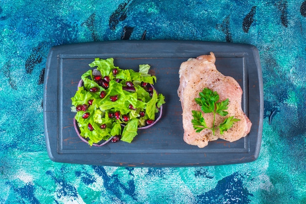 Gratis foto granaatappelpitten, slablaadjes met uienring naast kipfilet op een houten dienblad