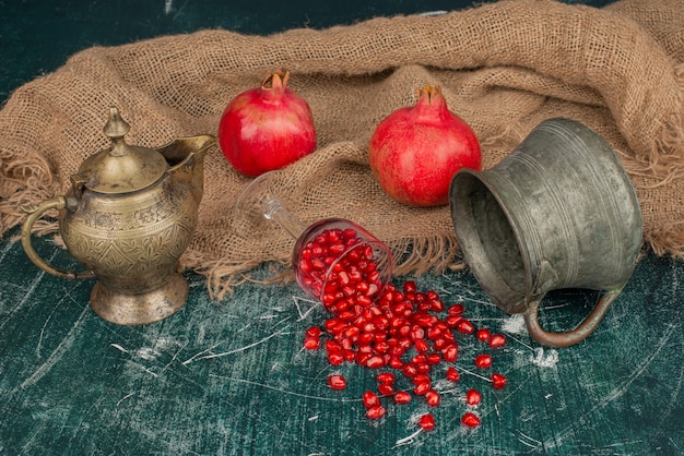 Granaatappelzaden die op marmeren tafel met vaas en theepot worden verspreid.