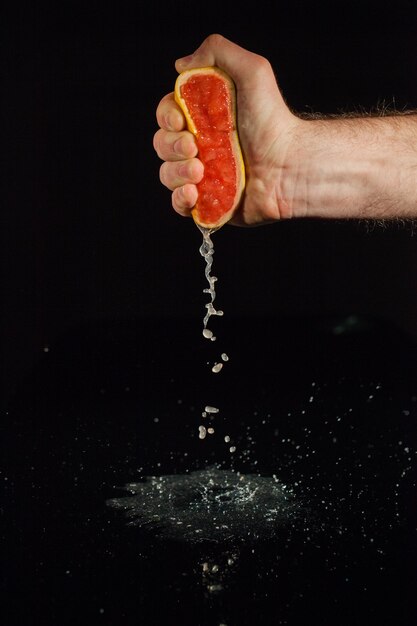Grapefruitensap spat uit de helft van het fruit dat in de hand van de mens wordt gehouden