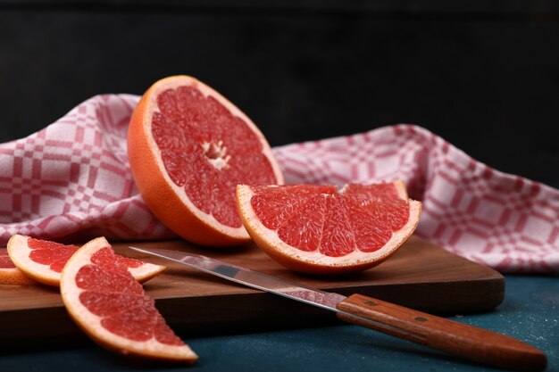 Grapefruitplakken op een houten raad op blauwe achtergrond en een mes.
