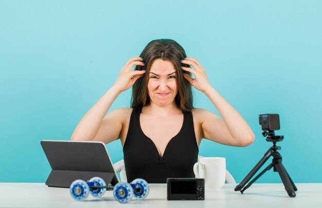Grappig bloggermeisje poseert voor de camera door haar hoofd te krabben op een blauwe achtergrond