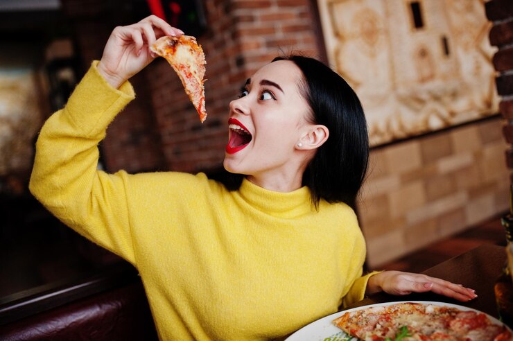 Grappig donkerbruin meisje die in gele sweater pizza eten bij restaurant