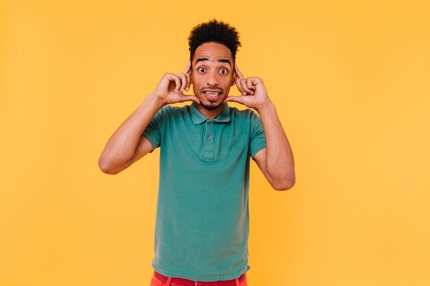 Grappig donkerogig mannelijk model dat met verbaasde gezichtsuitdrukking kijkt. Indoor portret van knappe verbaasde man in groen t-shirt.