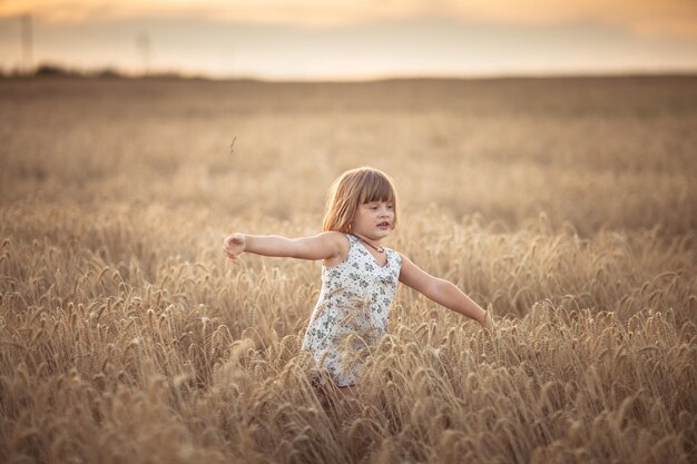 Grappig meisje danst in het veld met rogge bij zonsondergang