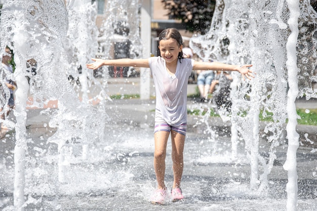Grappig meisje in een fontein, tussen de spatten van water op een hete zomerdag.