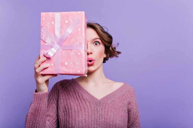 Grappig meisje in weelderige rok en witte hoed dansen Indoor portret van emotionele verrast vrouw in paarse trui poseren op donkere muur.