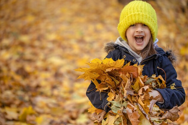 Grappig meisje met een bos herfstbladeren in het bos op een onscherpe achtergrond, kopieer ruimte.