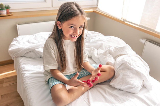 Grappig meisje met frambozen op haar vingers in bed in de ochtend