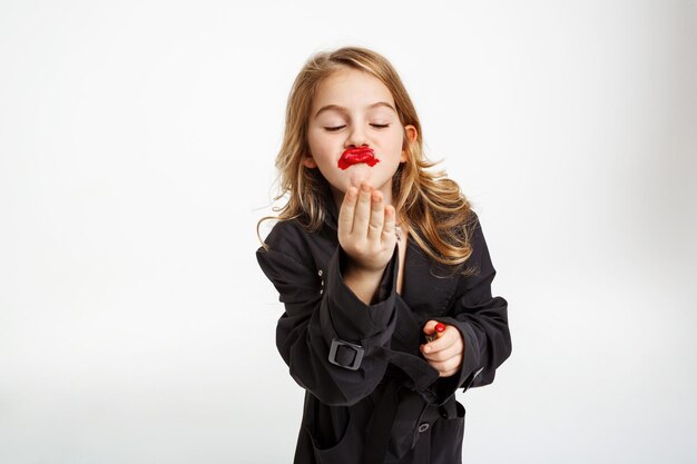 Grappig meisje met rommelige make-up. Het dragen van mode zwarte loopgraaf lucht zoenen, hoding rode lippenstift.