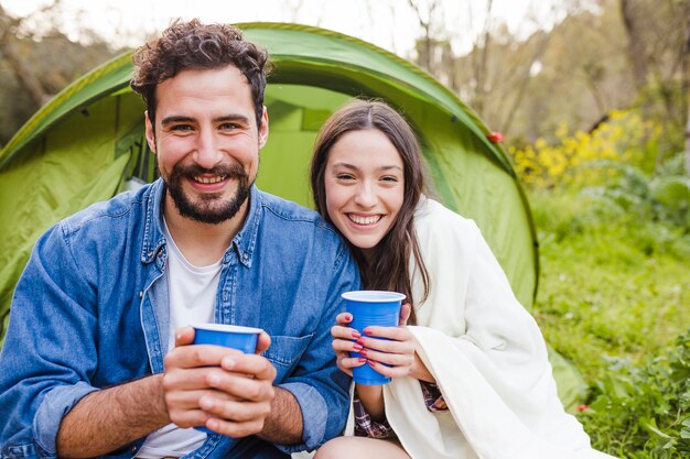 Grappig paar met kopjes in de buurt van tent