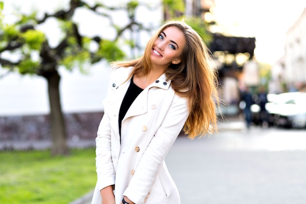 Grappig portret van gelukkig blond meisje, grappige gezichten maken en tong tonen op straat, herfsttijd, rust in de stad.