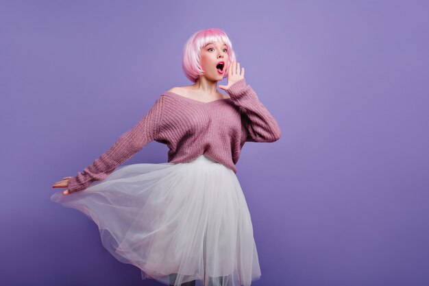 Grappig roze-haired meisje in periwig poseren Schattig vrouwelijk model draagt witte rok en heldere peruke genieten van fotoshoot.