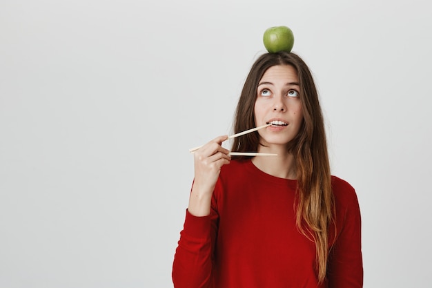 Grappig schattig meisje met appel op hoofd bijten stokjes, willen eten. Afhaal concept