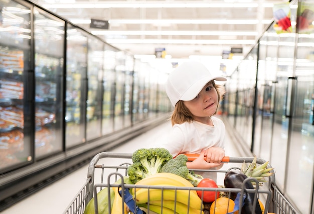 Grappig winkelend vrolijk mooi kind jongen in supermarkt koopt groenten gezond voedsel voor kind
