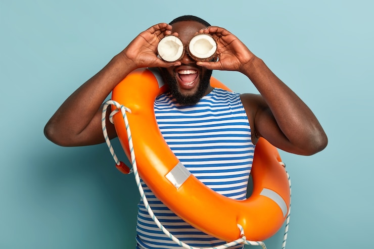Gratis Foto grappige donkere man heeft plezier alleen, houdt kokosnoten op de ogen, probeert afstand van het strand te kijken