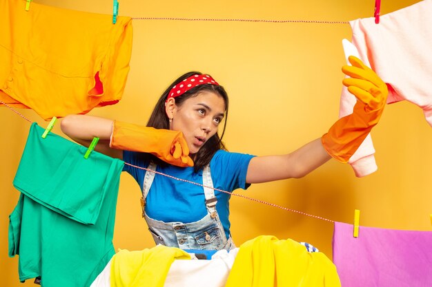 Grappige en mooie huisvrouw die huishoudelijk werk doet dat op gele achtergrond wordt geïsoleerd. Jonge blanke vrouw omringd door gewassen kleren. Huiselijk leven, heldere kunstwerken, huishoudelijk concept. Selfie maken.