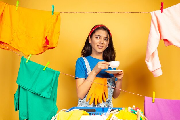 Grappige en mooie huisvrouw die huishoudelijk werk op gele achtergrond doet