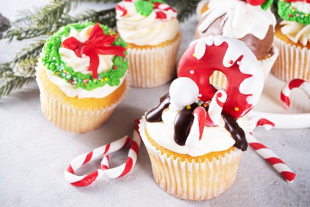Grappige kerst cupcakes. zelfgemaakte zoete cupcakes met suikerglazuur in vorm op kerstversiering en symbolen, op houten achtergrond met kerstdecor