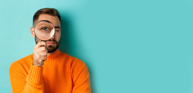 Gratis foto grappige man die door een vergrootglas kijkt en iets zoekt of onderzoekt dat in oranje staat