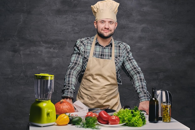 Grappige mannelijke chef-kok poseren in de buurt van de tafel met veel verse groenten.