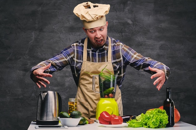 Grappige mannelijke chef-kok poseren in de buurt van de tafel met veel verse groenten.