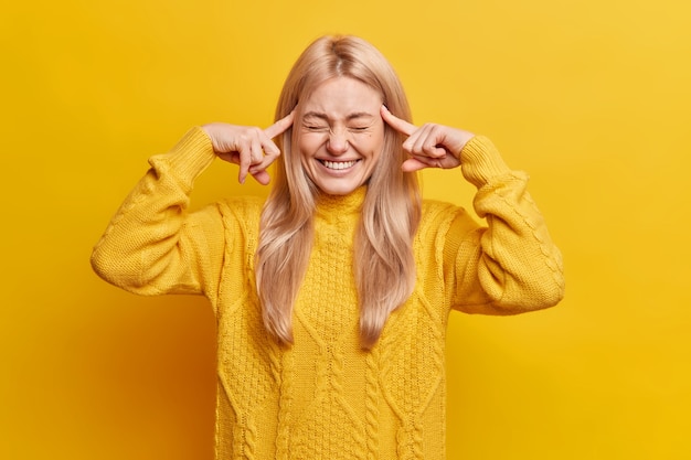 Grappige mooie blonde vrouw sluit de ogen en glimlacht in het algemeen houdt wijsvingers op tempels probeert iets te onthouden