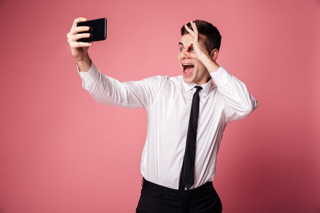 Grappige opgewonden jonge zakenman maken selfie via de mobiele telefoon