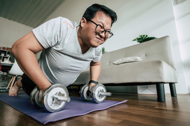 Grappige overgewicht man doet workout vetverbranding op sportmat met halters in push-up pose in woonkamer oefening voor gezonde kopieerruimte
