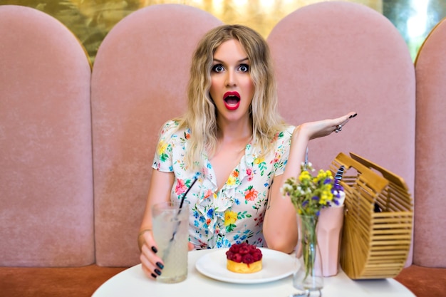 Gratis foto grappige stijlvolle portret van blonde vrouw die zich voordeed op schattig café eten dessert, gekke verrast emoties, dieet concept, pin-up stijl.