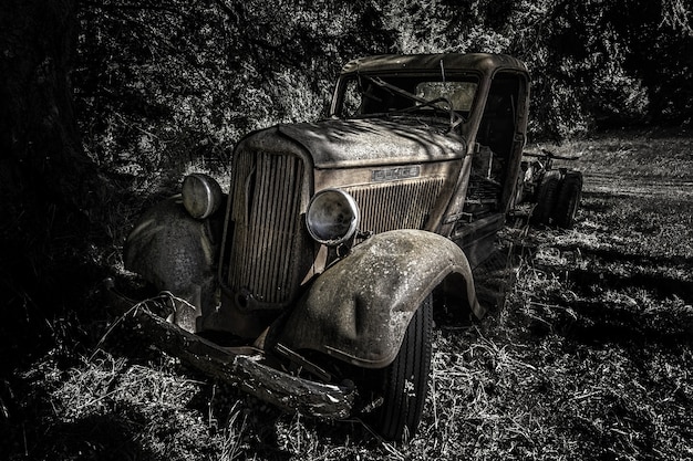 Greyscale die van een oude retro auto in het bos overdag is ontsproten