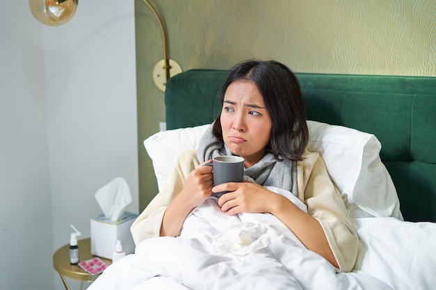 Griepziekte en mensen jonge vrouw die zich ziek voelt, koorts heeft en col oploopt terwijl ze warm in bed ligt