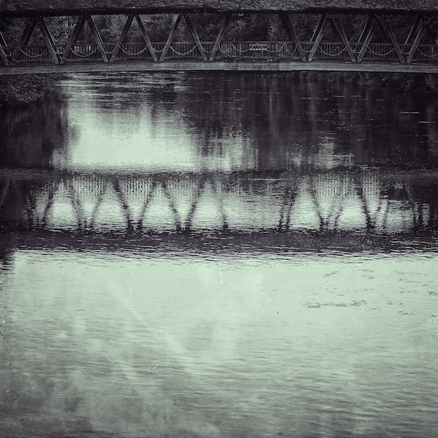 Gratis foto grijswaardenopname van de weerspiegeling van een houten brug in het water en de besneeuwde kust in de winter