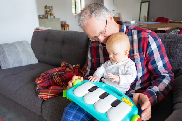 Grijze haren grootvader zittend op de bank en spelen met baby