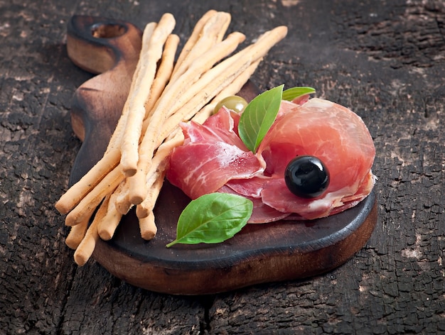 Gratis foto grissini-broodstokken met ham, olijven, basilicum op oude houten