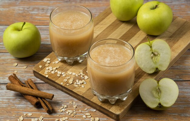 Groene appels, kaneelstokjes en twee kopjes vers sap op tafel, bovenaanzicht