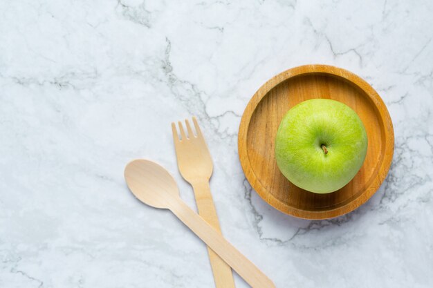 Groene appels zetten in een houten kom naast een houten lepel en vork