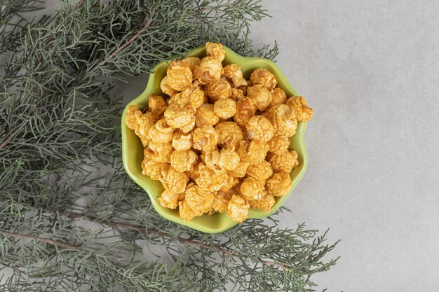 Groene bloemvormige kom vol karamelpopcorn genesteld tussen boomtakken op marmeren tafel.